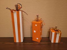 three orange and white wrapped gift boxes on a wooden table next to each other with polka dots