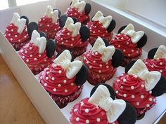 cupcakes with red frosting and white bows are in a box