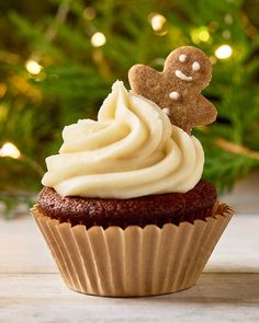 a cupcake with icing and a gingerbread man on top is sitting in front of a christmas tree