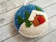 a felt ornament with a house and trees on it sitting on a wooden surface