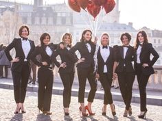 a group of women standing next to each other in front of a building with red heart balloons