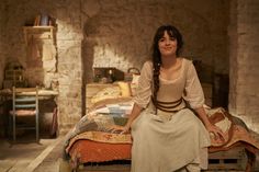 a woman sitting on top of a bed next to a stone wall in a bedroom