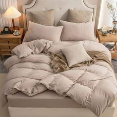 an unmade bed with pillows and blankets on it in a white room next to a lamp