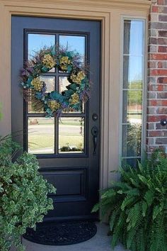 a black front door with a wreath on it and two plants next to the door