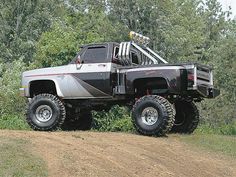 an off road truck is parked on the side of a dirt road in front of some trees