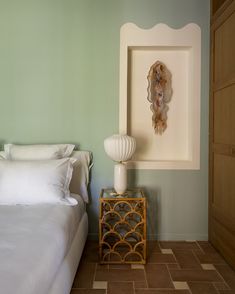 a white bed in a bedroom next to a wooden dresser and lamp on top of a tiled floor