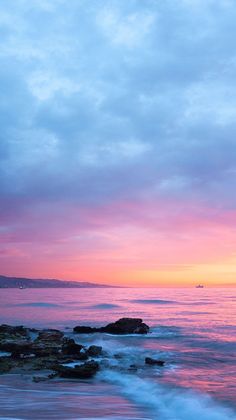 the sun is setting over the ocean with rocks in the foreground