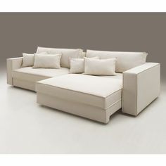 a white sectional couch with pillows on it's back and side facing the camera