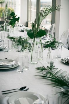 the table is set with clear vases and greenery