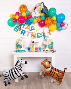 two zebras are standing in front of a birthday party table with balloons and streamers