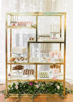 a display case filled with cakes and desserts on top of a wooden table covered in greenery