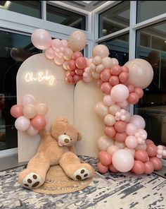 a teddy bear sitting in front of a balloon arch