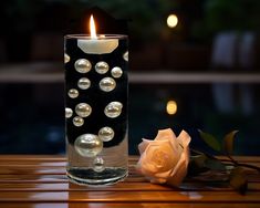 a candle that is sitting on a table next to a rose with pearls in it