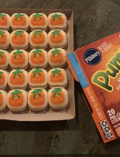 an open box of cookies with orange icing and green leaves on them next to a packet of dunkin'donuts