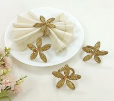 three napkins with gold sequin flowers on a white plate next to pink flowers