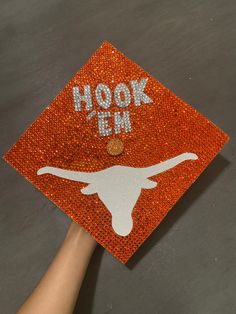 a hand is holding up an orange graduation cap with the word, hook in it