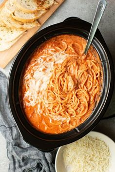 a crock pot filled with pasta and cheese on top of a wooden cutting board