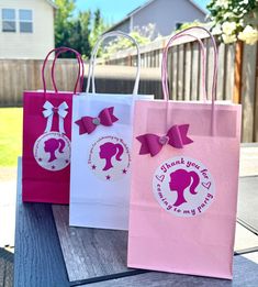 three pink and white shopping bags with bows on them sitting on a picnic table in front of a house