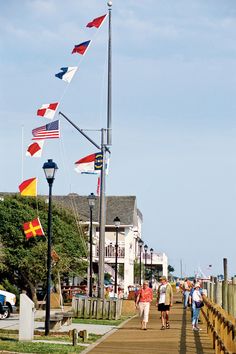 people walking on a boardwalk with flags flying in the wind