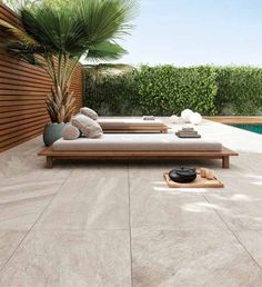 an outdoor lounge area next to a swimming pool and wooden fence with plants in the background