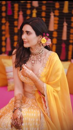 a woman in yellow dress sitting down with her hands on her chest and wearing jewelry