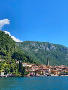 a town on the shore of a lake with mountains in the background and blue sky