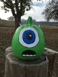 a green pumpkin with an evil eye painted on it's face sitting in front of a tree stump