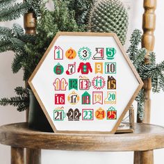 a cross stitch pattern on a wooden table next to a potted plant and pine tree