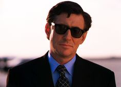 a man wearing sunglasses and a suit looks off into the distance