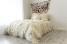 a bed with white fur on it in a room next to a window and wooden floor