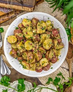 a white bowl filled with potato salad on top of a wooden table next to utensils