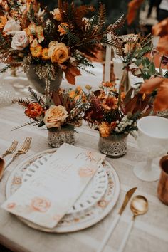 the table is set with orange flowers and white plates, silverware, and candlesticks