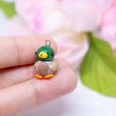 a tiny toy bird sitting on top of someone's finger in front of flowers