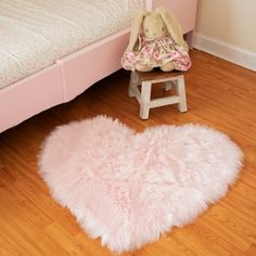 a teddy bear sitting on a stool in front of a pink heart - shaped rug