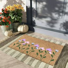 a door mat with flowers on it next to two pumpkins and potted plants