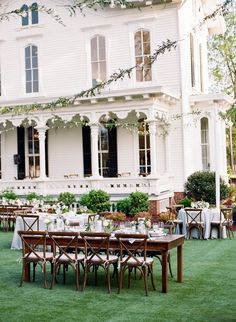 a large white house sitting on top of a lush green field with lots of tables and chairs