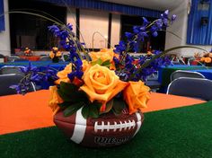 a football vase with flowers in it on top of a green carpeted table cloth