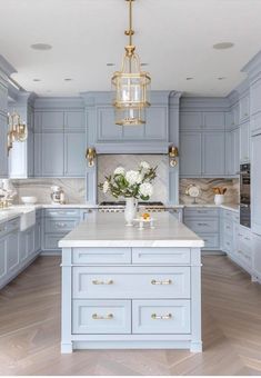 a large kitchen with blue cabinets and white counter tops, gold accents on the chandelier