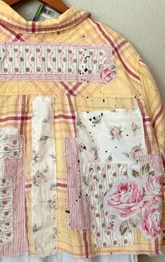 a yellow jacket with pink flowers on it hanging from a hanger next to a wall