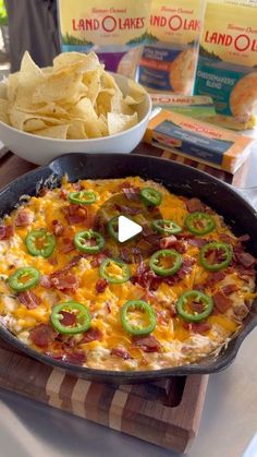 a skillet with cheese, bacon and jalapenos in it next to chips