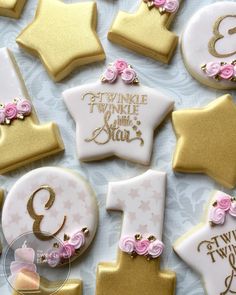 decorated cookies with pink and gold icing are arranged on a white tablecloth,