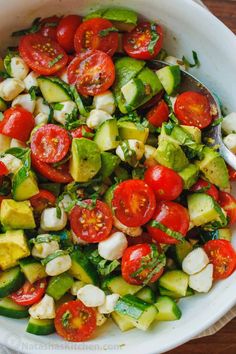 a white bowl filled with cucumber, tomato and avocado salad on top of a wooden table