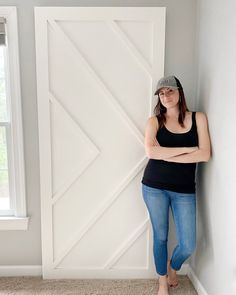 a woman leaning against a wall with her arms crossed and looking at the camera while wearing a baseball cap