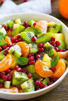 a white bowl filled with fruit salad on top of a wooden table next to oranges