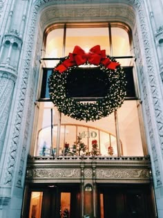 a christmas wreath hanging from the side of a tall building with red bows on it