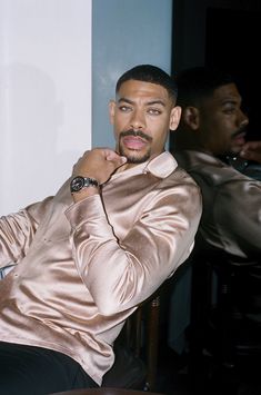 a man sitting down with his hand on his chin and looking at the camera while wearing a gold jacket