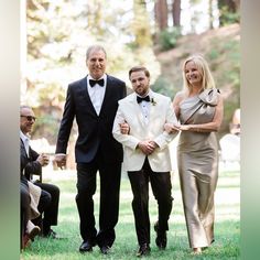 two men and a woman in formal wear standing next to each other on the grass