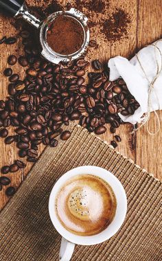 a cup of coffee sitting on top of a wooden table next to some coffee beans