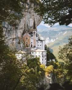 an old church built into the side of a mountain in europe, surrounded by trees