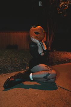 a woman sitting on the ground wearing a pumpkin mask